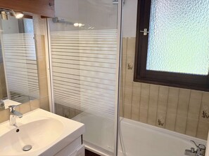 A bathroom with a white sink, a mirror, a shower enclosure, and a window with blinds.