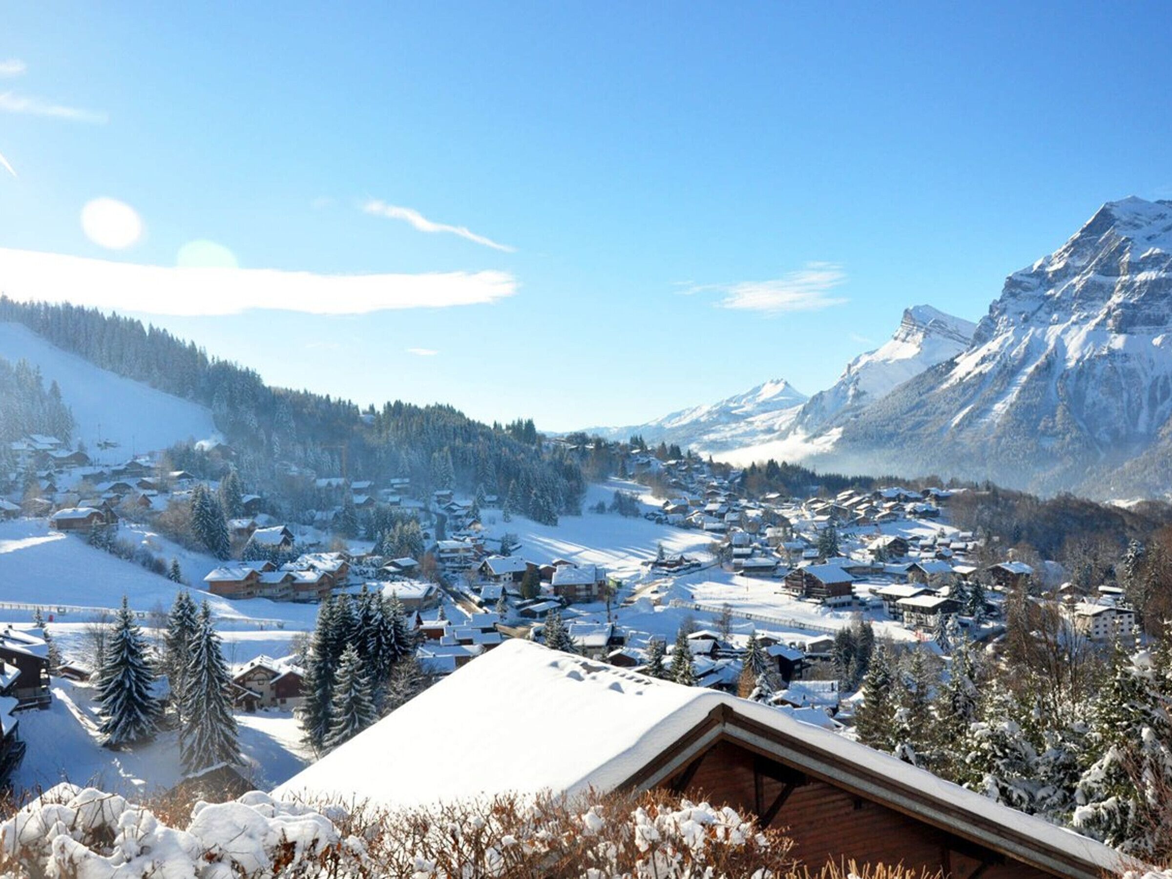 A snow-covered village with traditional wooden houses, a mountain backdrop, and a clear sky.
