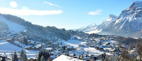 A snow-covered village with traditional wooden houses, a mountain backdrop, and a clear sky.