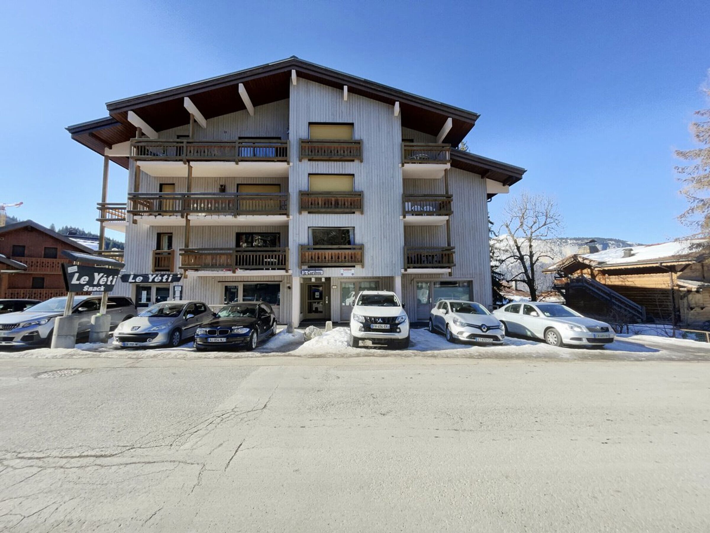 A multi-story building with balconies, a sign for 'Le Yeti Snack', and several cars parked in front.
