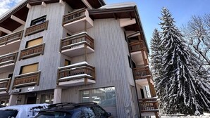 A multi-story building with balconies, a sign reading "Le Caribou," and a snow-covered tree in the background. - Renovated 2-Room Ski-In/Ski-Out Unit, Sleeps 6, Near Shops & Services (Les Carroz d'Arâches)