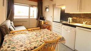 A compact kitchen with a dining area, a dishwasher, and a window with curtains. - Renovated 2-Room Ski-In/Ski-Out Unit, Sleeps 6, Near Shops & Services (Les Carroz d'Arâches)
