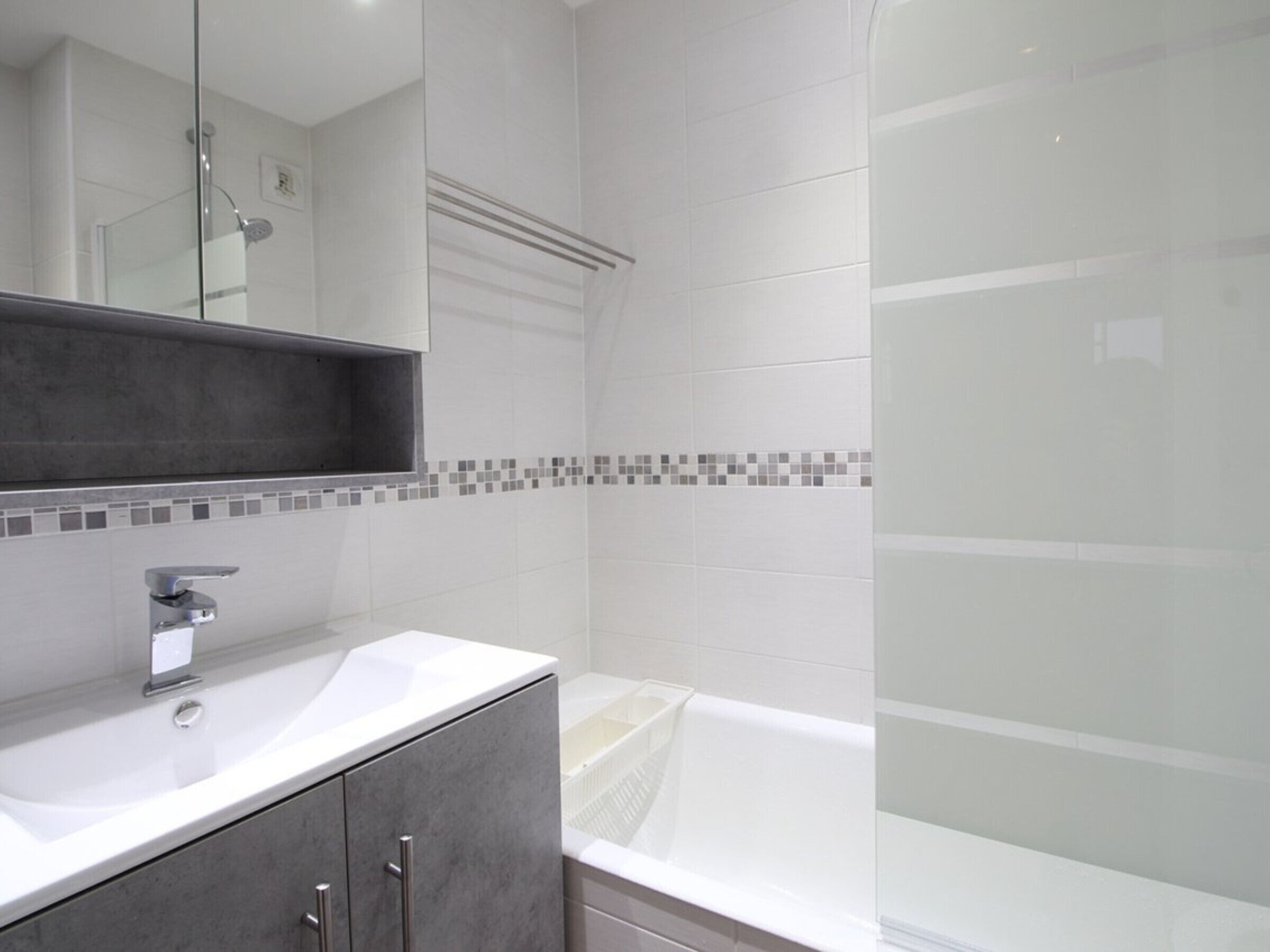 Un baño moderno con lavamanos blanco, espejo y cabina de ducha.