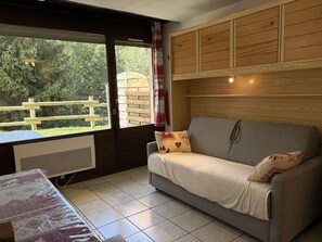 Une pièce chaleureuse avec un canapé gris, un meuble en bois et une fenêtre donnant sur une terrasse en bois.