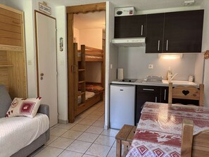 A compact room with a bunk bed, a small kitchenette, a dining table, and a sofa with a cushion. - Studio Central pour 4 Pers. à Proximité des Pistes et des Commerces, avec Terrasse (Les Carroz d'Arâches)