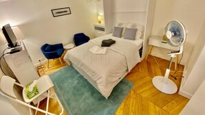 Quarto com cama, escrivaninha, cadeira, espelho e ventilador.
