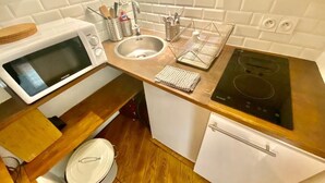 Cozinha equipada com micro-ondas, pia e fogão. Possui bancada de madeira e armário branco.
