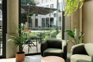 Un área de estar moderna en el interior, con un amplio ventanal, una planta en maceta y una mesa de madera.