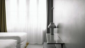 A hotel room with a bed, a bedside table with a lamp, and a window with curtains.