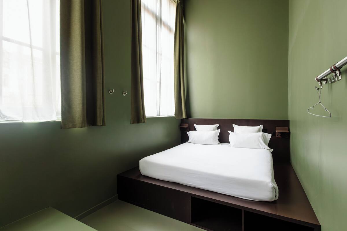 Ein Schlafzimmer mit einem Bett, Vorhängen, einem Nachttisch und einer Wandleuchte.