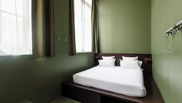 Une chambre à coucher avec un lit, des rideaux, une table de chevet et un luminaire fixé au mur.