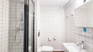 A modern bathroom with white tiled walls, a glass shower enclosure, a white toilet, and a white sink with a mirror above it.