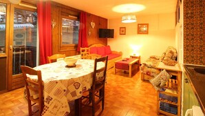 A cozy living room with a dining area, wooden flooring, a sofa, a TV, and a kitchen area with a sink and cabinets. - Studio for 6 people with renovated bathroom and parking, on the slopes (Les Carroz d'Arâches)