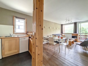 A modern kitchen with wooden cabinets, a dishwasher, and a dining area with white chairs and a table.