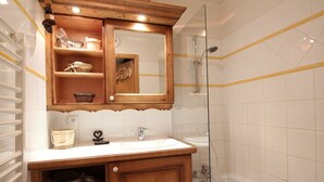 Un baño con tocador de madera, espejo, lavabo y ducha con mampara de vidrio.