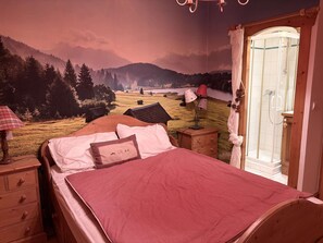 Een slaapkamer met een bed, nachtkastje, lamp, houten dressoir en een douche.