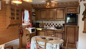 Una cocina acogedora con armarios de madera, una mesa de comedor con mantel floral y una tetera roja.
