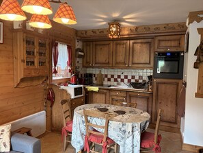 Een gezellige keuken met houten kastjes, een eettafel met bloemenlaken en een rode waterkoker.