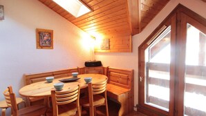 A cozy dining area with a wooden table and chairs, a bench, and a large window with a view. - Mezzanine studio for 5, at the foot of shops, 450m from slopes (Les Carroz d'Arâches)