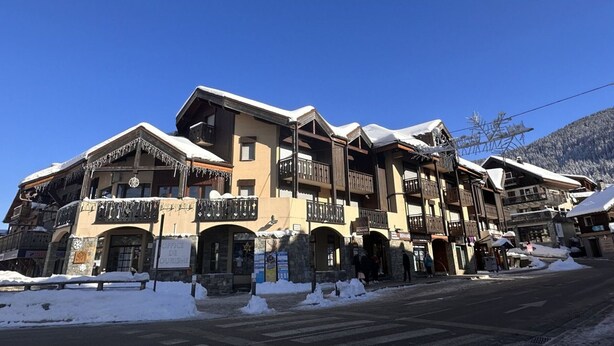 A traditional chalet-style building with multiple balconies and a stone facade, surrounded by snow. - Mezzanine studio for 5, at the foot of shops, 450m from slopes (Les Carroz d'Arâches)