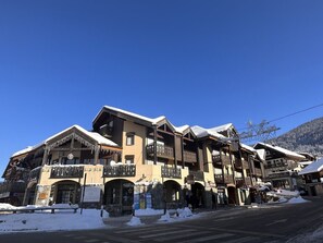 A traditional chalet-style building with multiple balconies and a stone facade, surrounded by snow. - Mezzanine studio for 5, at the foot of shops, 450m from slopes (Les Carroz d'Arâches)