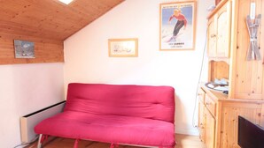 A cozy room with a red sofa, wooden walls, a wooden cabinet with skis, and a poster of a skier. - Mezzanine studio for 5, at the foot of shops, 450m from slopes (Les Carroz d'Arâches)