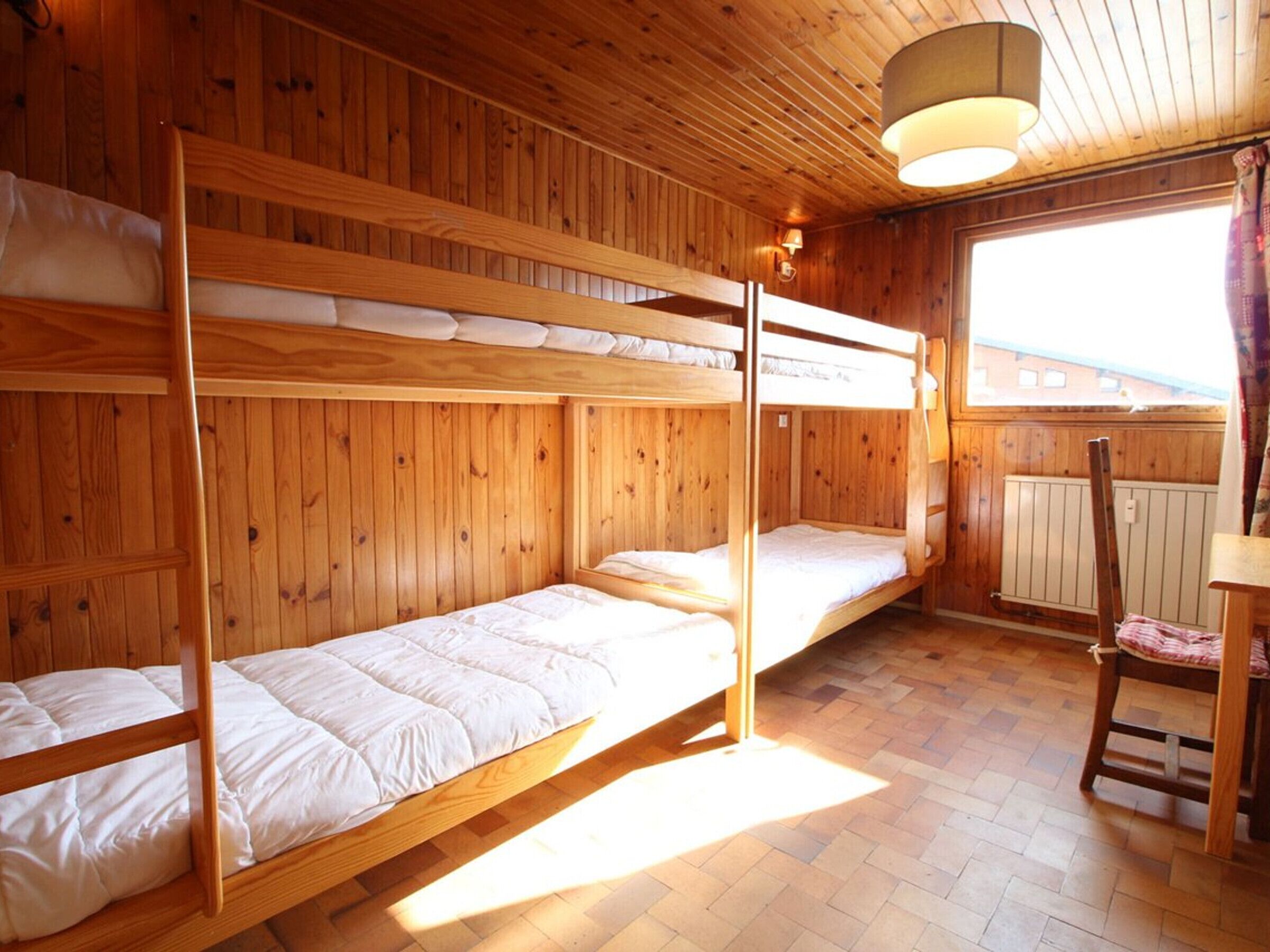 A wooden cabin room with bunk beds, a chair, and a window with a view.