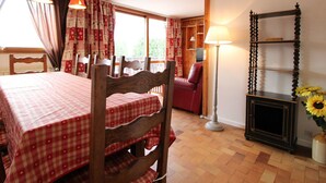 Un coin repas avec une nappe à carreaux, des chaises en bois, un fauteuil rouge, une lampe et une bibliothèque.