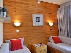 Une pièce aux murs recouverts de lambris en bois, deux lits avec une literie rouge et blanche, une petite table de chevet avec une lampe et un tableau encadré accroché au mur.