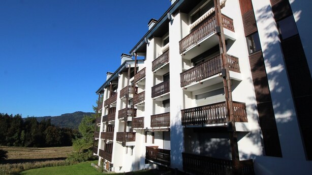 Ein mehrstöckiges Hotel mit Balkonen, umgeben von einer Rasenfläche und Bäumen.