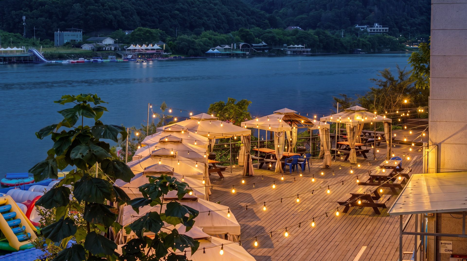 An outdoor dining area with string lights, umbrellas, and tables overlooking a body of water.