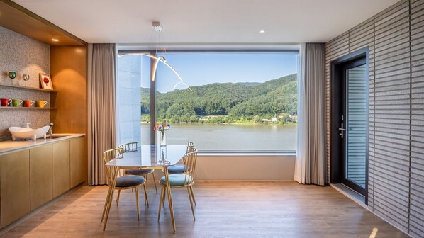 Una cocina moderna con un ventanal grande, una zona de comedor con mesa y sillas, y vistas a un lago y colinas.
