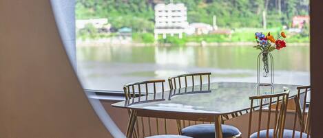 A round table with chairs, a vase with flowers, and a view of a lake with buildings in the background.