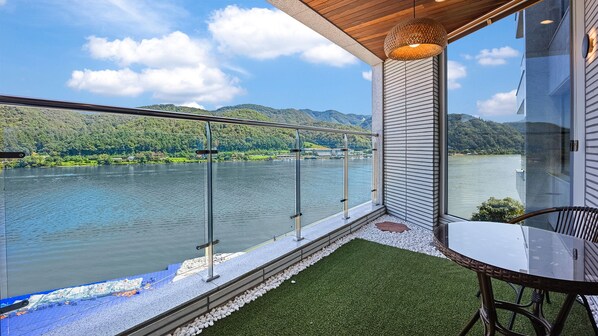 Un balcon doté d’une balustrade en verre donnant sur un lac, une table avec des chaises et une vue sur le paysage environnant.