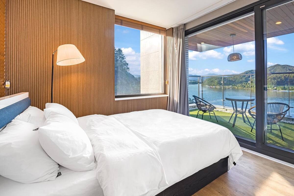 Ein Schlafzimmer mit einem großen Bett, einem Fenster und einem Balkon mit Tisch und Stühlen mit Blick auf einen See.