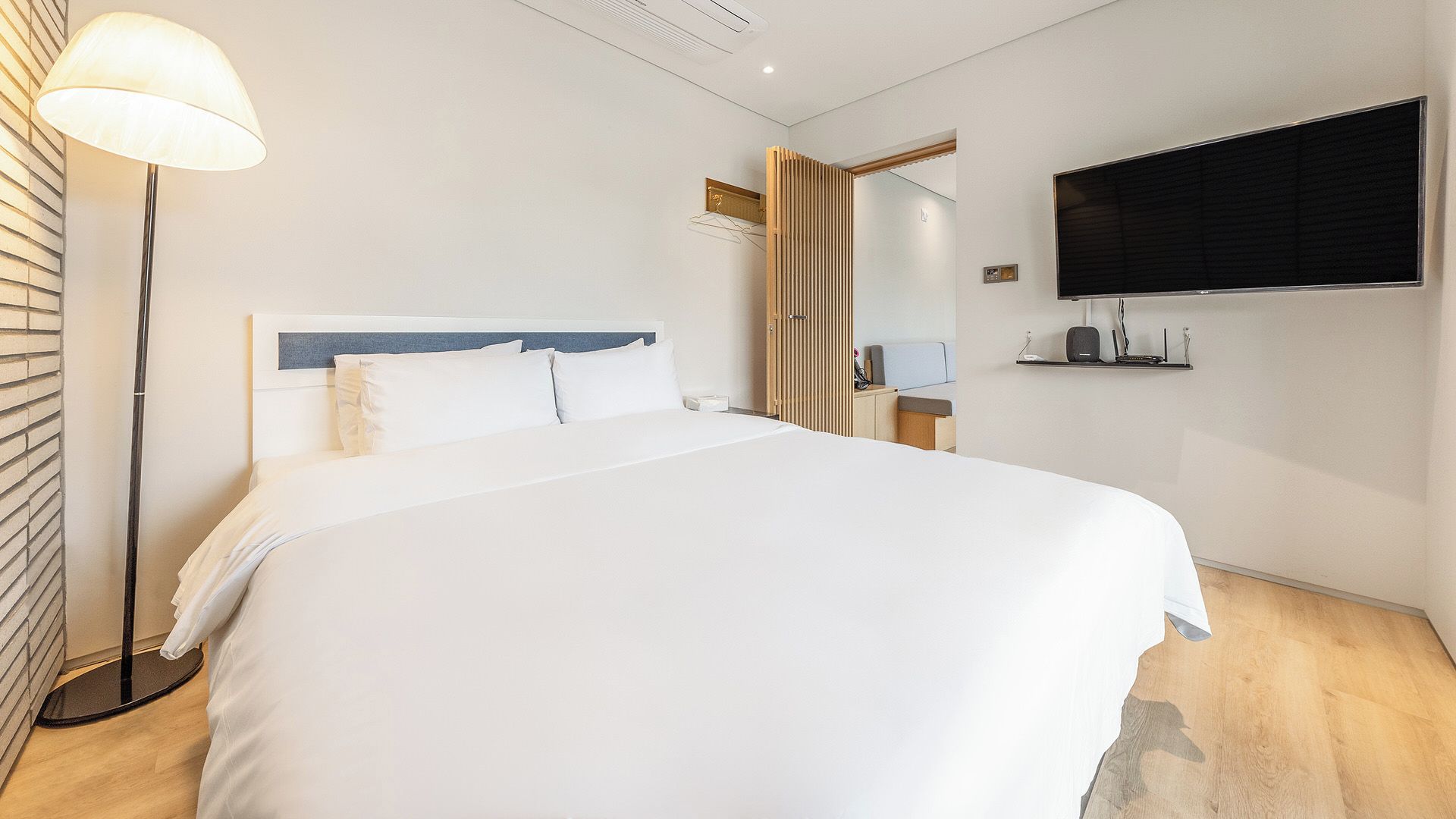 A hotel room with a bed, a bedside table, a lamp, a TV mounted on the wall, and a wooden wardrobe.