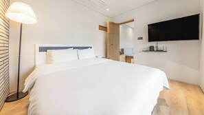 Habitación de hotel con cama, mesita de noche, lámpara, televisor montado en la pared y armario de madera.