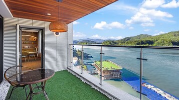 Un balcón con vista a un lago y montañas, una silla de mimbre y una mesa con sillas.