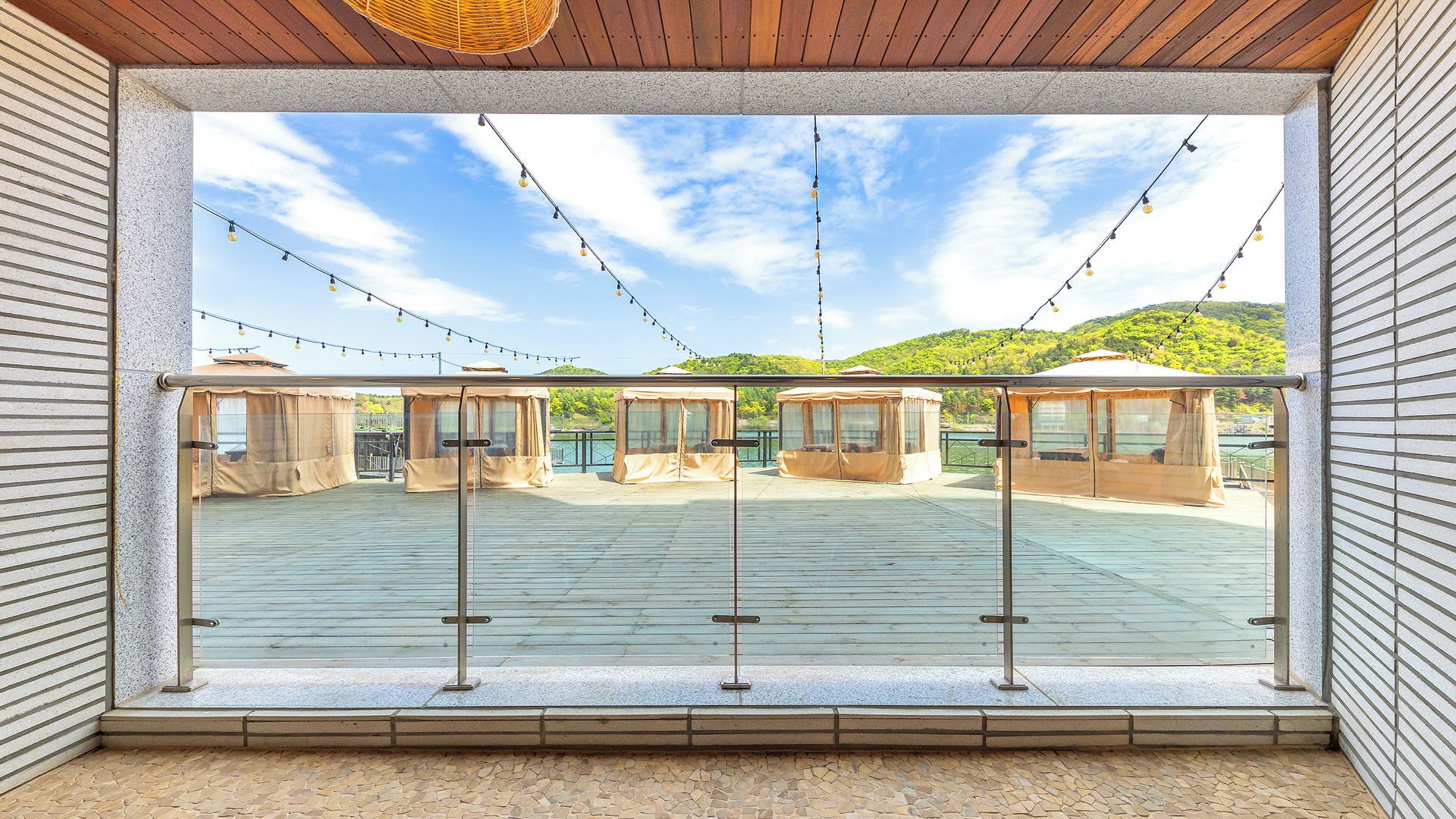 A covered outdoor deck with string lights, a glass railing, and covered seating areas.