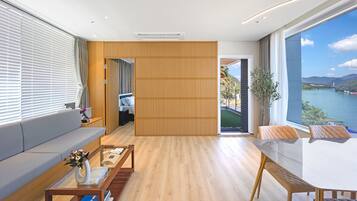 Une chambre d’hôtel moderne avec un plancher en bois, une table basse en verre, un canapé, une table à manger et une vue sur un lac.