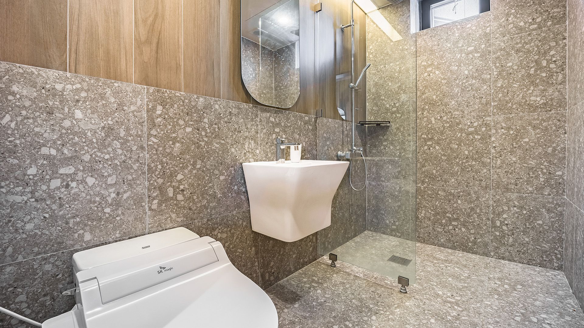 A modern bathroom with a white sink, a glass shower enclosure, and a toilet.