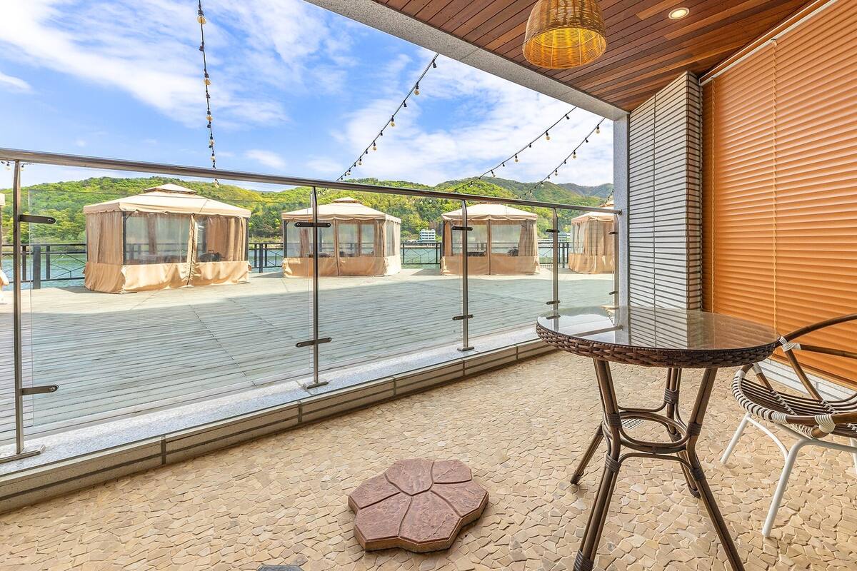 Ein Balkon mit Tisch und Stühlen mit Blick auf einen Poolbereich, der überdachte Sitzgelegenheiten und eine Aussicht auf grüne Hügel bietet.