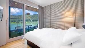 Un dormitorio con una cama grande, vista a un lago y montañas a través de una puerta corrediza de vidrio, y una lámpara fijada a la pared.