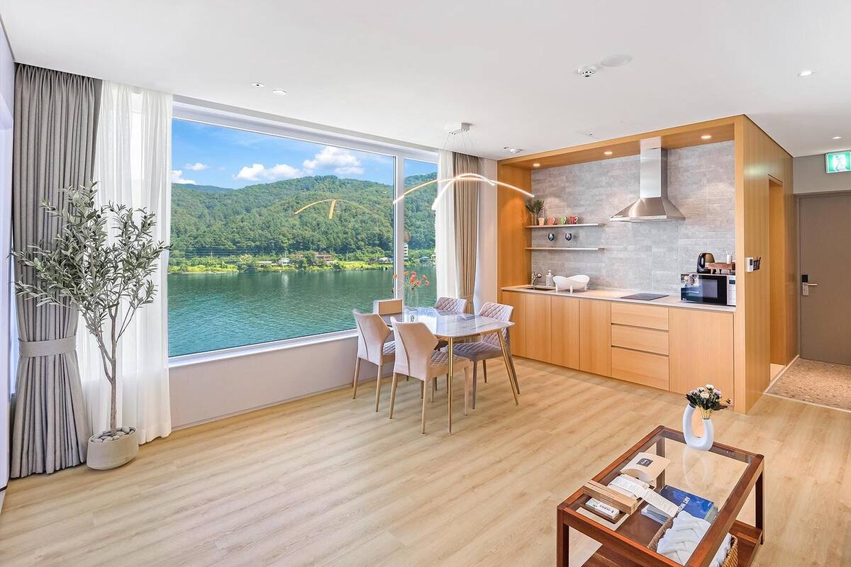 Ein modernes Hotelzimmer mit Essbereich, Küchenzeile und großem Fenster mit malerischem Seeblick und Bergblick.