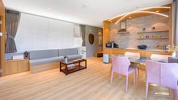Ein modernes Wohnzimmer mit Sofa, Couchtisch und Sesseln. Es gibt eine Küchenzeile mit Herd, Spüle und Regalen.