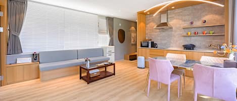 A modern living room with a sofa, coffee table, and chairs. There is a kitchen area with a stove, sink, and shelves.