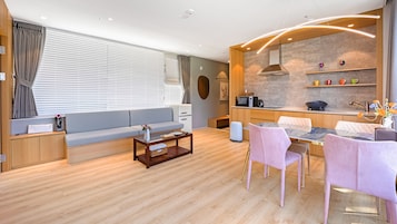 Una sala moderna con sofá, mesa de centro y sillas. Hay una cocina con estufa, fregadero y estanterías.