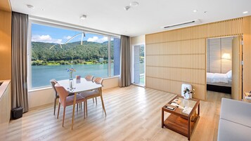 Habitación de hotel con mesa de comedor, sillas, una mesita de centro, una cama y vistas a un lago y bosque.