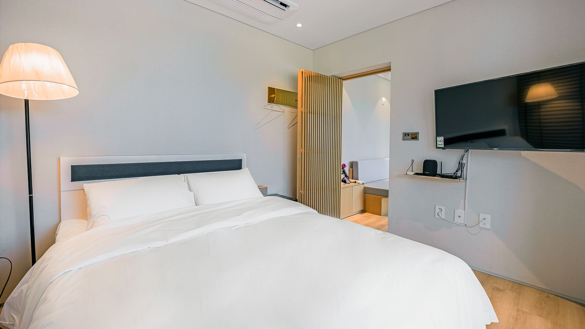 Una habitación de hotel con una cama, un televisor montado en la pared y una lámpara.