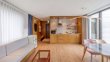 Et moderne hotelværelse med tekøkken, opholdsområde med sofa og glasbord, samt et stort vindue med udsigt.